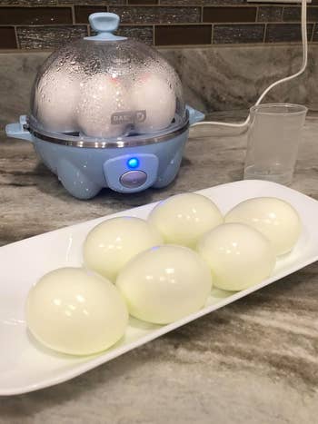 reviewer's light blue egg cooker with eggs in it and boiled eggs in front of it on a plate