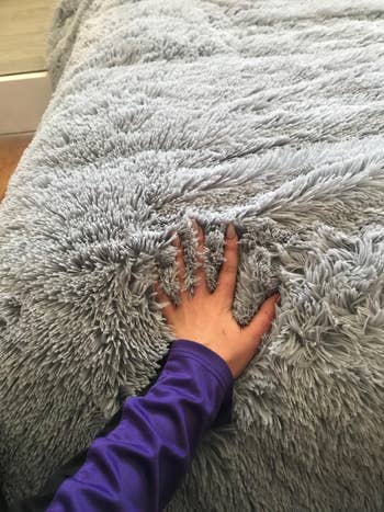 a reviewer pressing their hand into a shaggy gray comforter