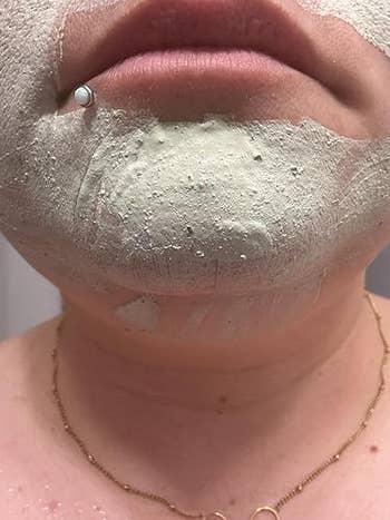 A idiosyncratic   applying a clay look   mask, focusing connected  the chin area, with a articulator  piercing and a elemental  necklace visible