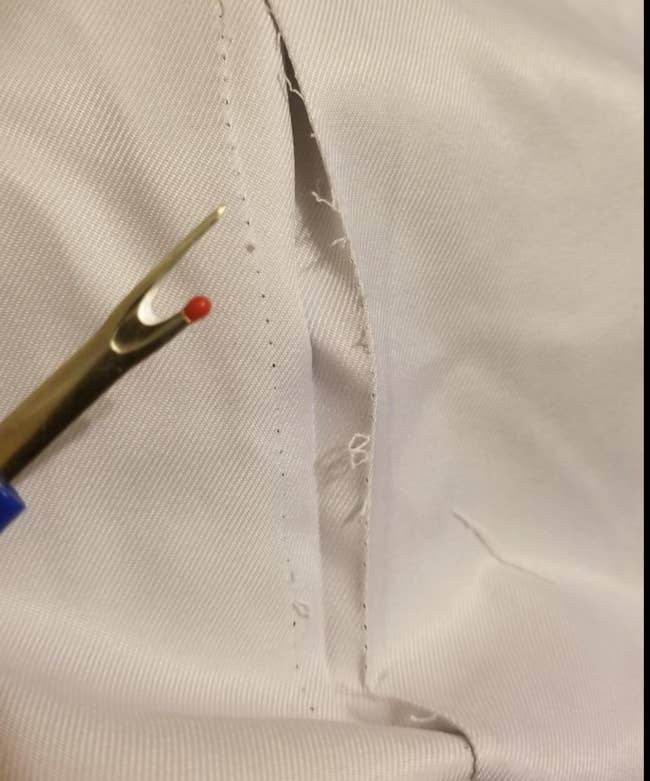 Reviewer holding the small tool with a sharpened point next to ripped out seams from a blanket 