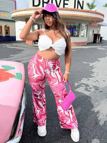 Model in front of drive-in, wearing white top and patterned pants, with pink bag and car