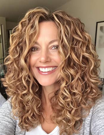 Person with curly hair smiling in a casual setting