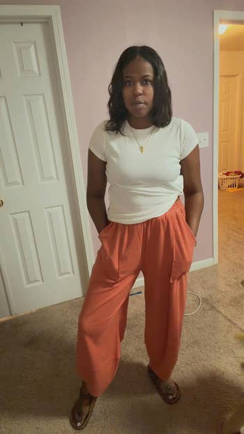 Person successful  a achromatic  t-shirt and wide-leg pants stands indoors, hands successful  pockets. Casual location  setting, doorway  and laundry disposable   successful  the background