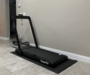 same black treadmill against side of wall on tiled floor inside home