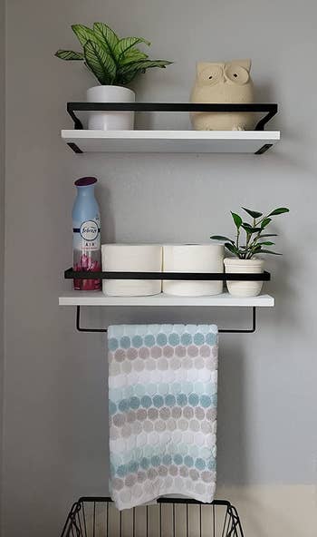 Reviewer image of white wood and black metal shelves mounted on a gray wall with towel hanging on hood and toiletries lined along the products
