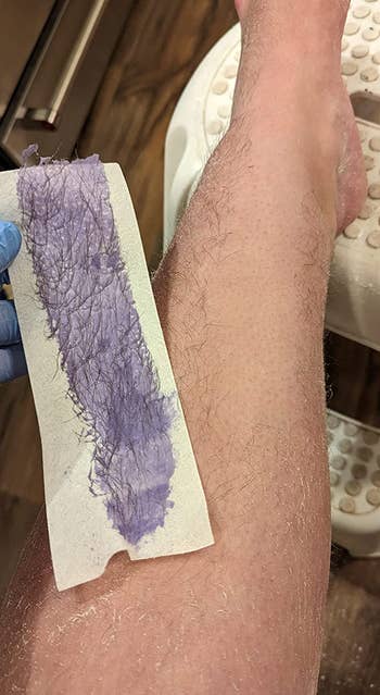reviewer holding wax strip with purple wax and hair on it