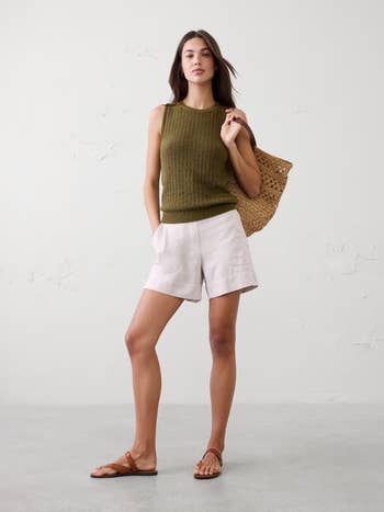 Woman successful sleeveless knit top, linen shorts, holding a woven tote, wearing sandals. Casual summertime fashion