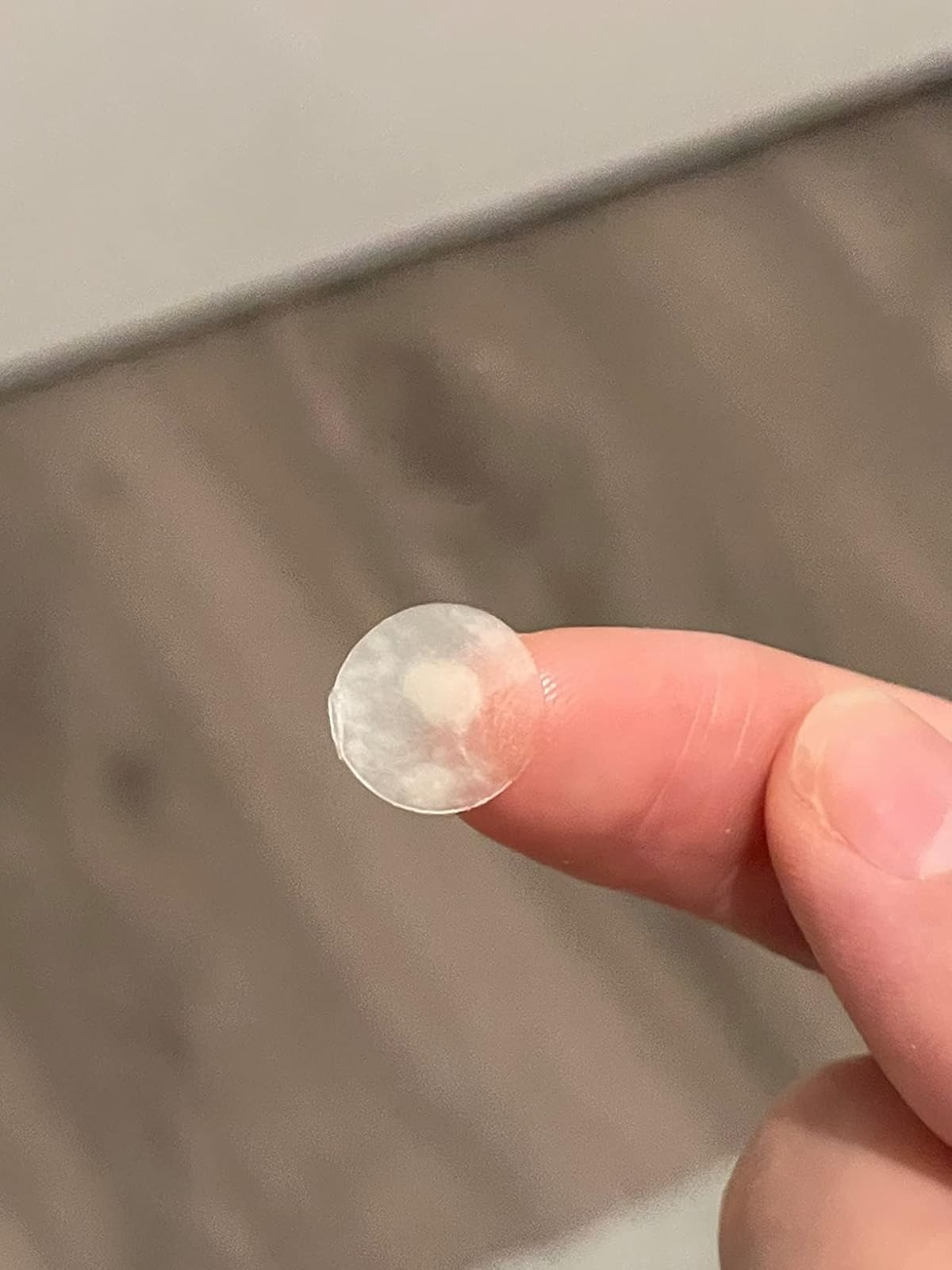Close-up of a fingertip holding a small used acne patch