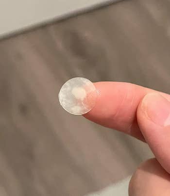 Close-up of a fingertip holding a small used acne patch