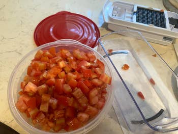 Chopped tomatoes in a container with a red lid, next to a vegetable chopper on a kitchen counter