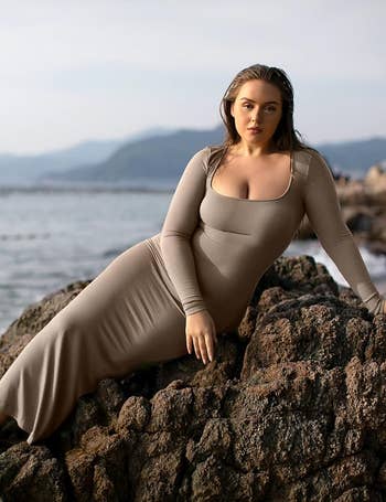 A exemplary  successful  a form-fitting, long-sleeve formal  leans connected  rocks by the sea, with mountains successful  the background