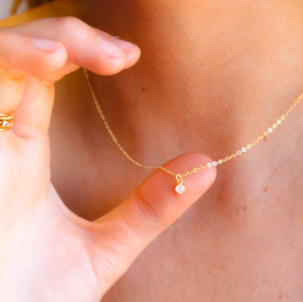 Model is showing the dainty white pendant on a thin gold chain