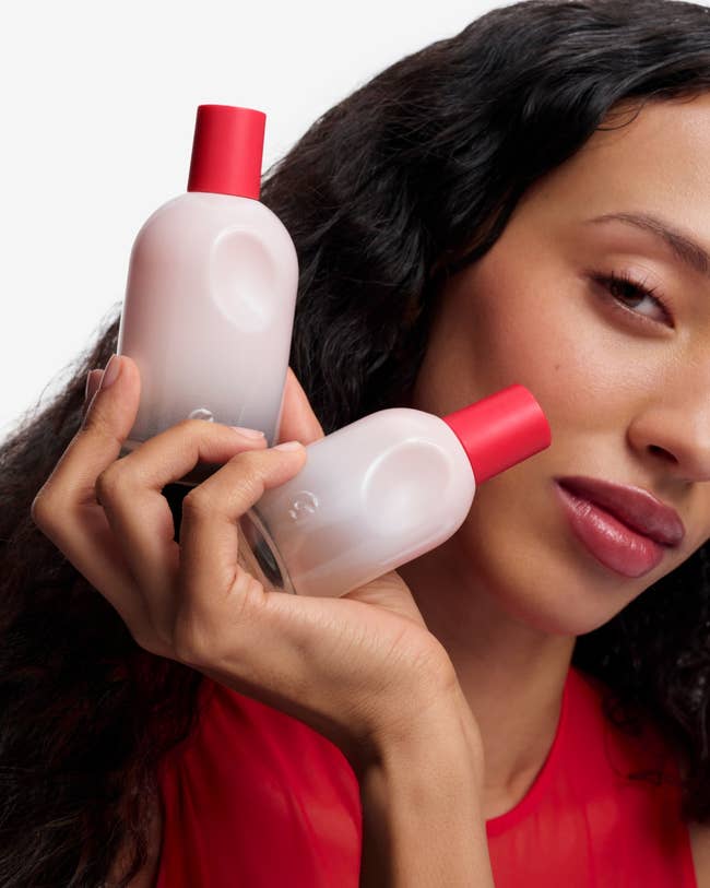 Person holding 2  skincare bottles with reddish  caps, posing for a quality   merchandise  advertisement