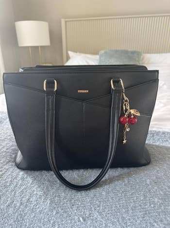 Elegant handbag with dual handles and a cherry-themed charm hangs on the side, resting on a textured surface in a room setting