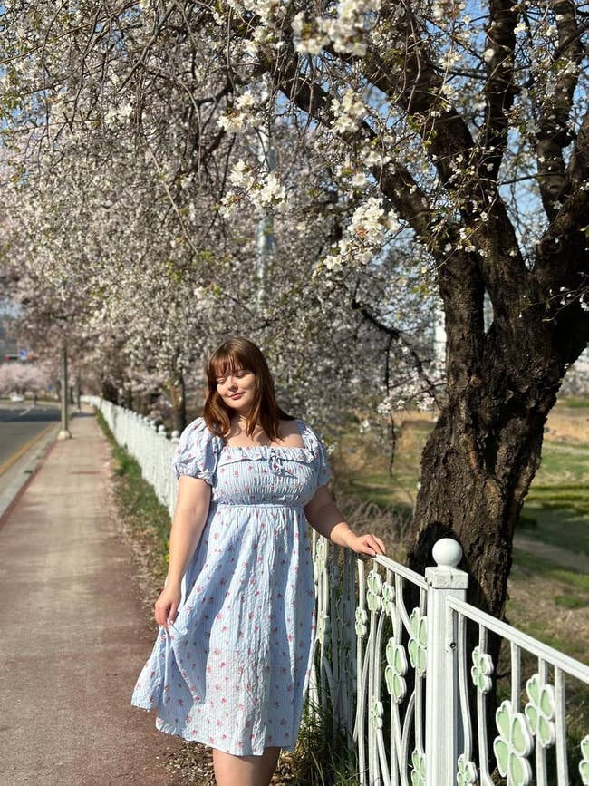 Person successful  floral formal  stands by a obstruction   lined with blooming trees, enjoying a outpouring  time  outdoors
