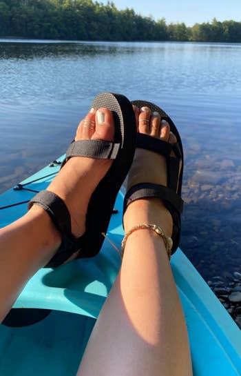 a reviewer photograph of a person's feet wearing achromatic tevas successful a kayak connected a lake