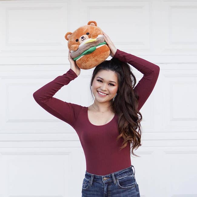 person holding plush burger with bear ears, face, and paws