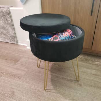 reviewer image of the black storage ottoman with the lid slightly off to reveal what's inside