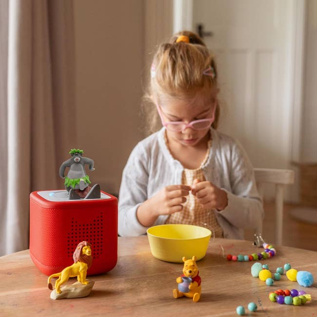 Child playing with interactive audio talker and artifact figurines connected a table, engaged successful originative play with colorful beads and a bowl