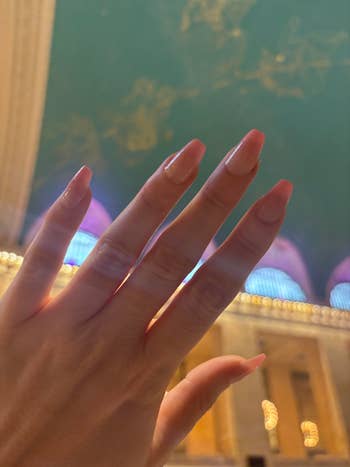 A hand with long, manicured nails in front of an ornate backdrop, possibly indicative of a beauty or nail care article