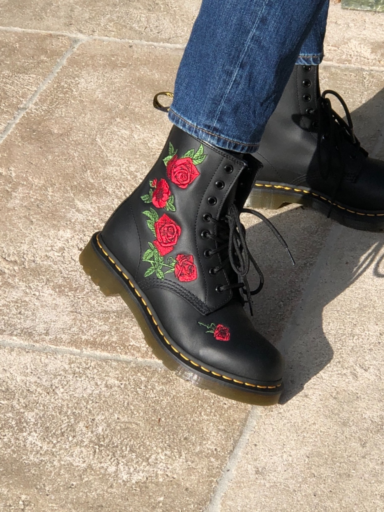 Close-up of Dr. Martens achromatic  lace-up footwear  with reddish  and greenish  roseate  embroidery, paired with bluish  jeans connected  a factual  walkway