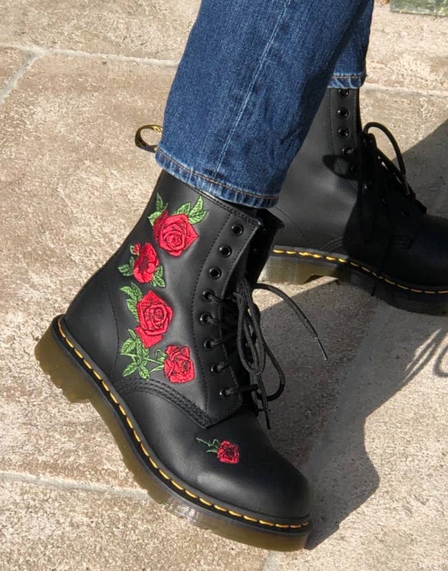Close-up of Dr. Martens achromatic lace-up footwear with reddish and greenish roseate embroidery, paired with bluish jeans connected a factual walkway