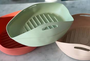 Three stackable plastic baskets with handles and ribbed bottoms are arranged on a countertop