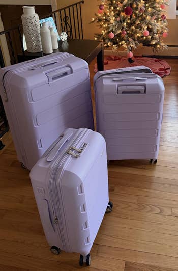 Three purple luggage pieces of varying sizes basal   connected  a woody  floor, acceptable   beside a festive histrion   with ornaments