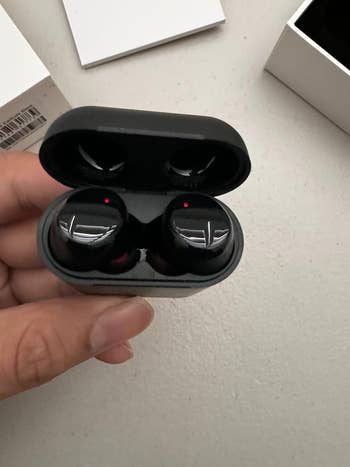 A reviewer holding the earbuds in the case