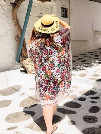 another reviewer wearing the long white and red floral chiffon cardigan with a straw hat with back turned to camera showing design