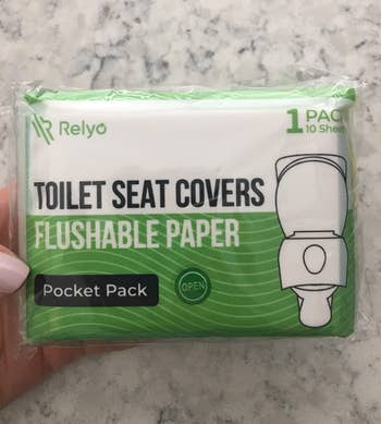 image of reviewer's hand holding up pack of flushable toilet seat covers