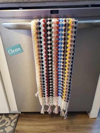 A colorful patterned crocheted towel hangs over a dishwasher handle with a 