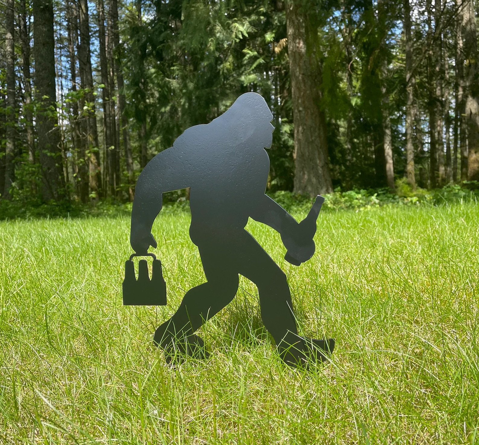 Black metal outlined big foot stake placed in grass outside in front of trees