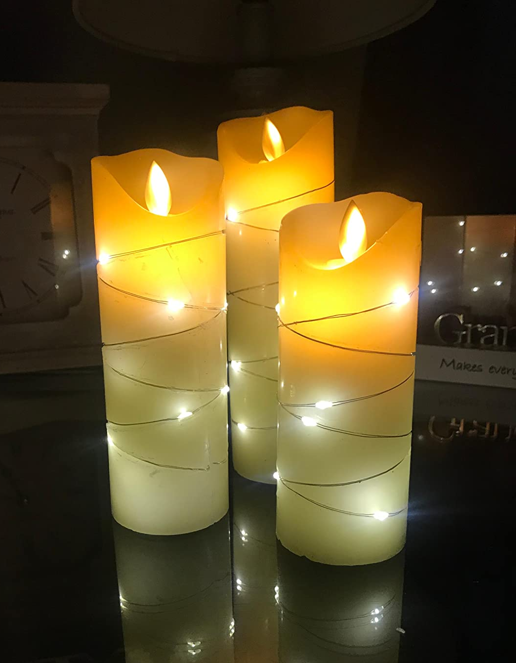 Reviewer image of three white flameless candles with twinkle lights wrapped around them on top of a black table and turned on