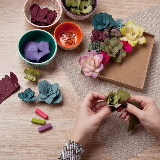 a person making a felt succulent on a table full of other felt succulents