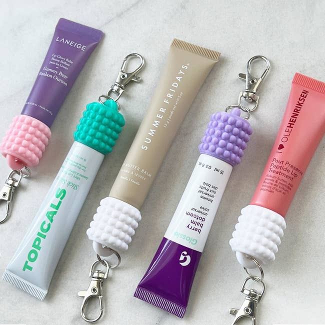 Laneige, Summer Fridays, Ole Henriksen lip products in tubes with keychain holders on a marble surface