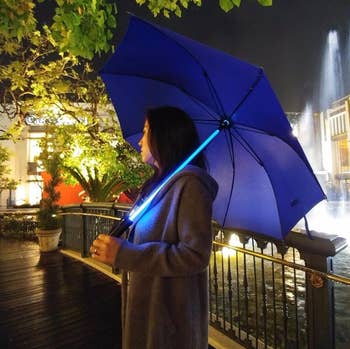 A reviewer holding the umbrella, in blue which has a shaft that glows like a lightsaber 