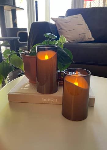 Two lit candles successful  brownish  solid  holders connected  a publication  with a works  and sofa successful  the background