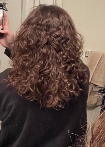 same reviewer's hair after using the product, with less frizz and more defined curls 