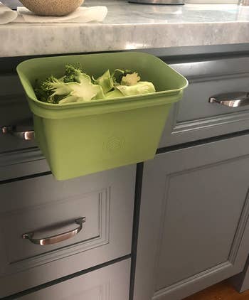 reviewer photo of the green bin attached to the side of their counter and holding discarded broccoli stems