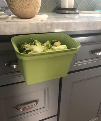 reviewer photo of the green bin attached to the side of their counter and holding discarded broccoli stems