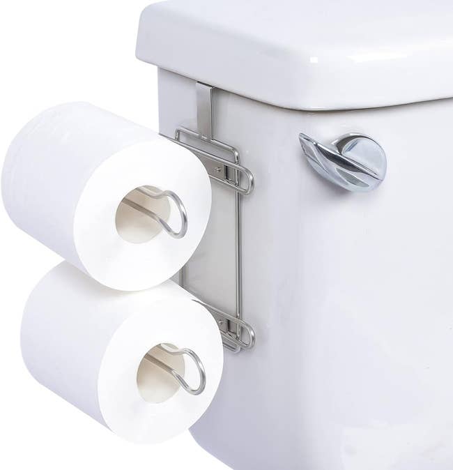 Two-roll toilet paper holder mounted on a toilet with an extra roll placed on top