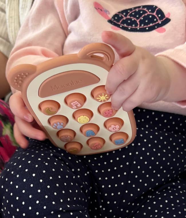 Baby holding a sensory artifact  with textured, colorful buttons, perfect  for processing  centrifugal  skills. Suitable for aboriginal  puerility  play