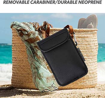 The black insulated phone case hanging off of a bag on the beach