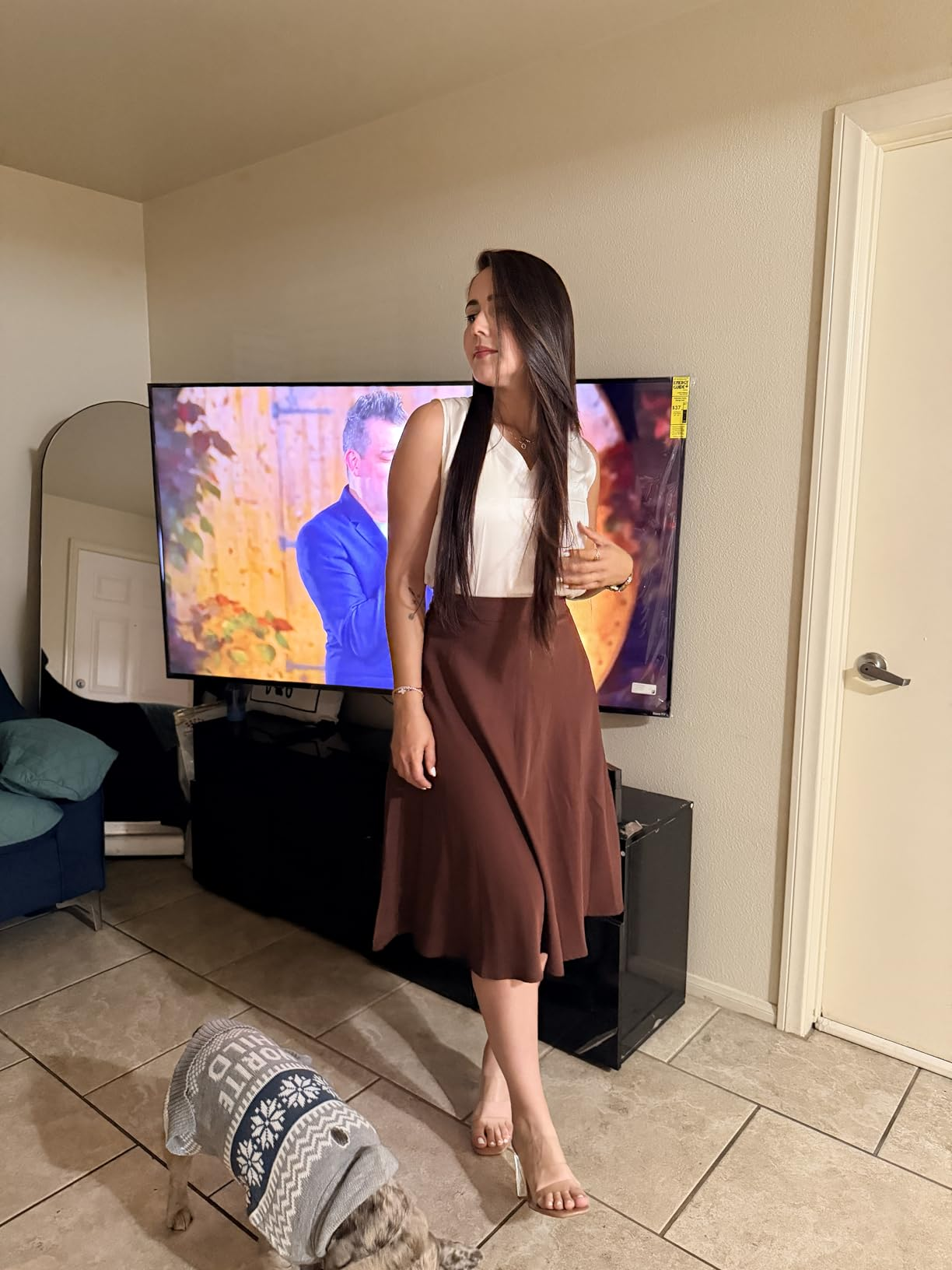 Reviewer successful  a stylish sleeveless formal  poses successful  a surviving  room; a canine  with a sweater is nearby. 