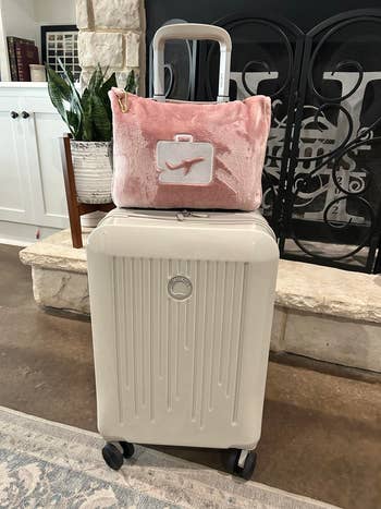 reviewer photo of the pink blanket and pillow wrapped up in its carrying case and attached to the handle of their suitcase