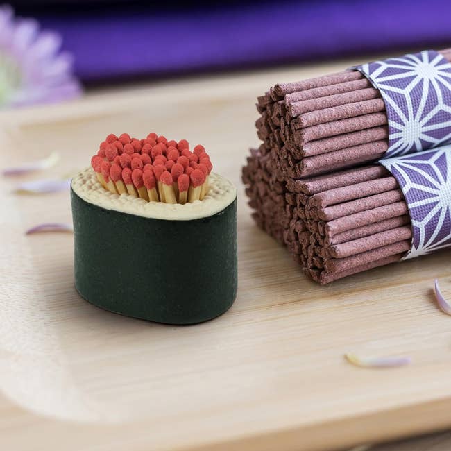 Sushi-shaped decorative point  with matchsticks resembling roe adjacent  to a bundle of incense sticks connected  a woody  surface