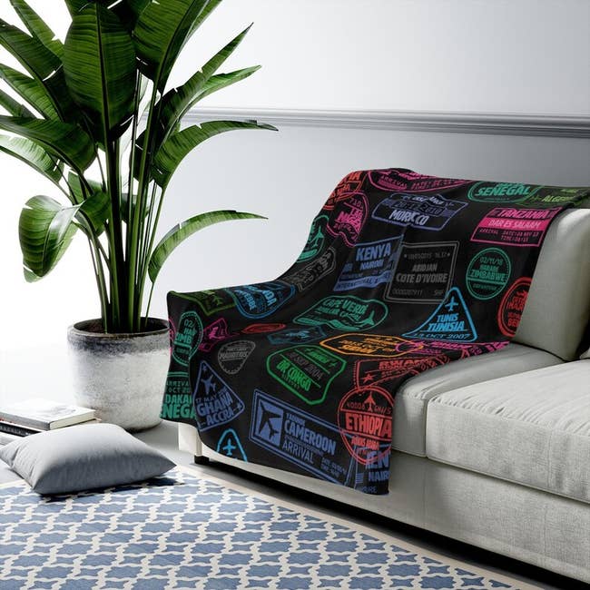 A sofa with a blanket featuring travel-themed patterns in a modern living room setting