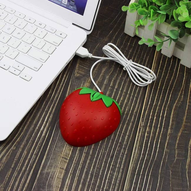 Strawberry-shaped mouse next to a laptop and plant on a desk