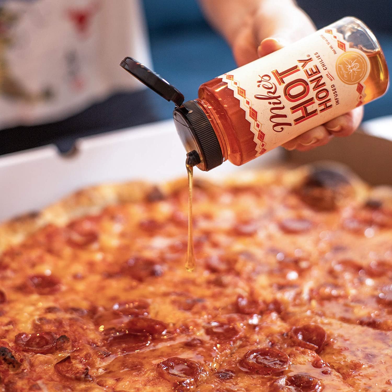 Hand drizzling Mike's Hot Honey on a pepperoni pizza